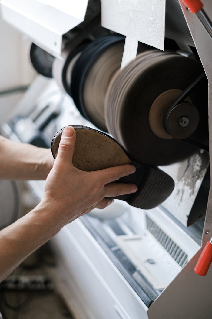 Detailed view of hands sanding a shoe sole in an industrial workshop. Perfect for illustrating craftsmanship.